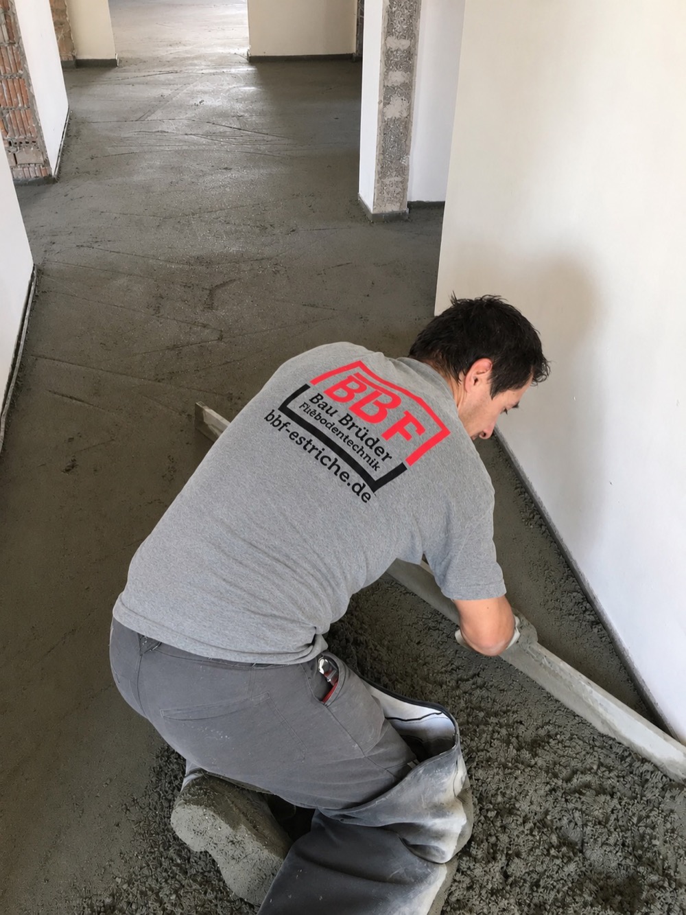 BBF-Mitarbeiter glättet frisch eingebrachten Heizestrich entlang der Wand